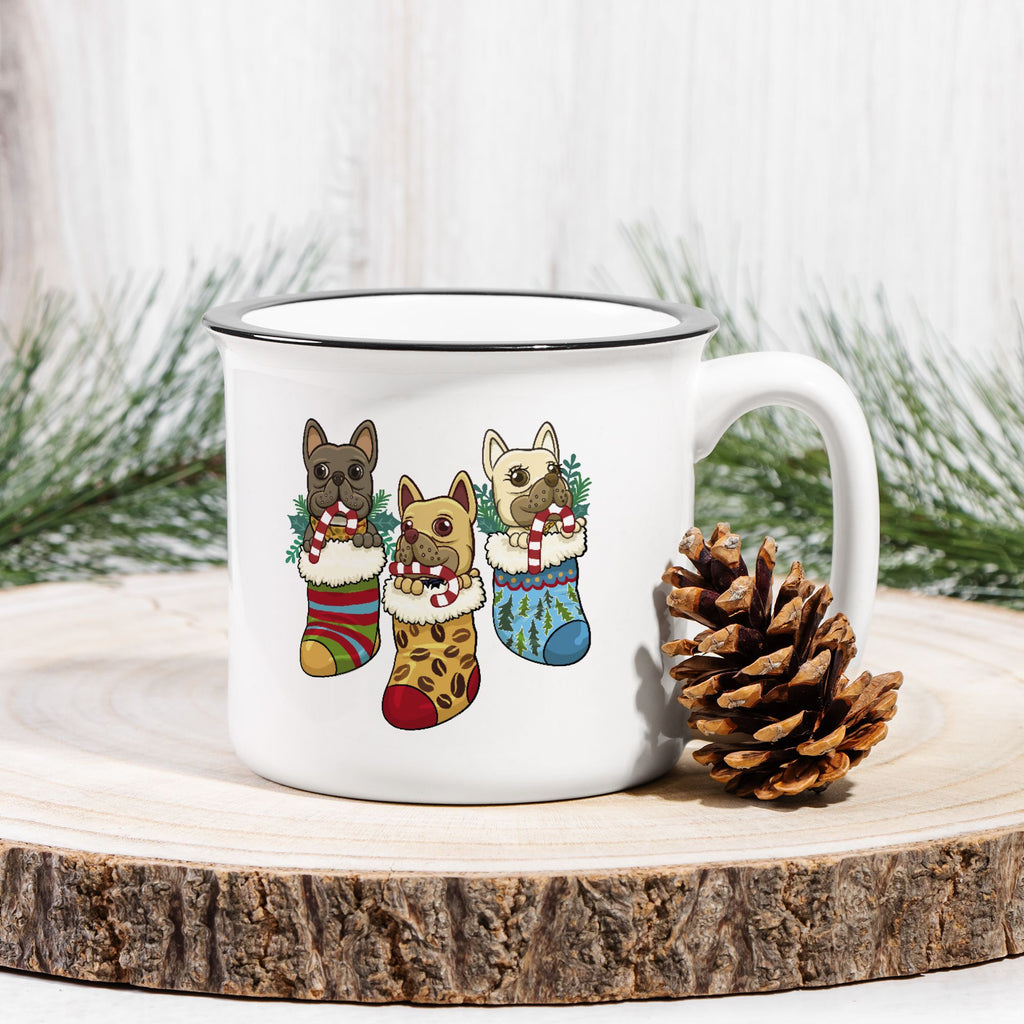 White mug with Christmas-themed dog illustrations on a wooden surface with pine cones and branches.